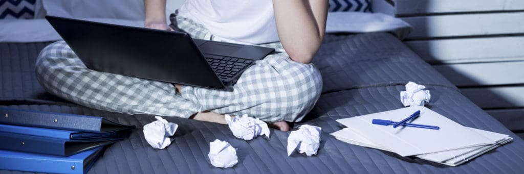 A stressed student is studying on a laptop and multiple crumpled wads of paper